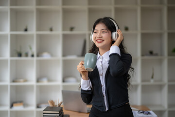 Beautiful Asian woman wearing headphones enjoying music and holding a hot drink. Relax with coffee...