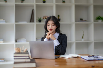 Fototapeta na wymiar Freelance Asian woman sitting and working on laptop. Thinking, planning and focusing on the task.