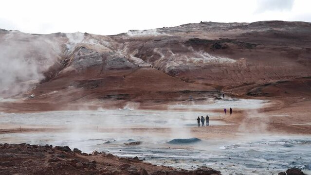 Námafjall Geothermal Area. Tourists stroll among steaming fumaroles and boiling mud pots. Panorama of suggestive volcanic landscape. Sulfurous mud springs, solfataras and steam springs. 4k slow motion