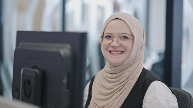 In a modern office, a Muslim entrepreneur wearing a hijab sits confidently and diligently works on her computer, embodying determination, creativity, and empowerment in the business world