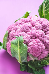 Fresh organic purple cauliflower cabbage with leaves on lilac background, top view