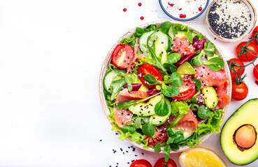 Keto salad with salted salmon, avocado, tomatoes, lettuce, cucumber, sesame seeds. Low-carbohydrate breakfast rich in healthy fats. White table background, top view