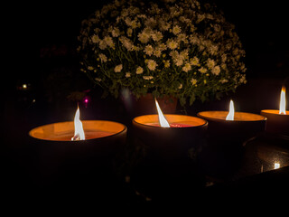 trzy ceramiczne znicze płonące na nagrobku stojące obok kwiecistej chryzantemy - obrazy, fototapety, plakaty