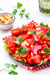 Exotic salad with watermelon, tomatoes, onion, salted peanuts and parsley on white table background, top view