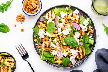 Tasty fresh salad with grilled zucchini, feta cheese, walnuts, red onion and spinach on white table background, top view