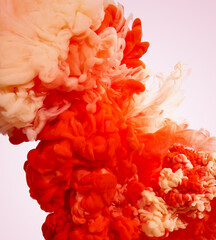 Paint drops of red and beige pigments in water on pink background
