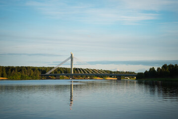 Fototapeta na wymiar A calm view of a bridge in the city of Rovaniemi. Traveling north, outdoor recreation, polar circle, tourism in Lapland. Bridge with lumberjack candle. River near the forest. Quiet place for relax