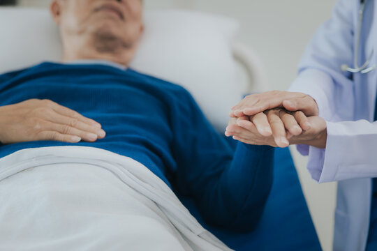 Beautiful Asian female doctor in white top talking with senior patient at bedside in hospital or clinic ward