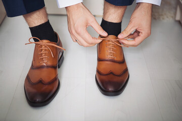 Male businessman puts on stylish shoes. man getting ready for work,groom morning before wedding...