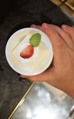 Too view of kid hand holding a panna cotta cake decorated by strawberry