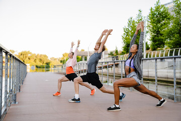 Group of three active people doing stretching exercises outdoors on bridge