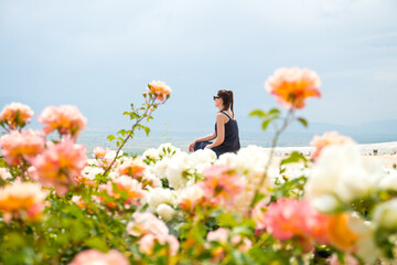 Girl or woman sits on a terrace with a panoramic view of the mountains with pink roses rosebuds in...