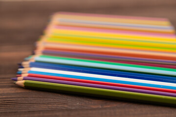 Set of watercolor pencils on brown wooden. Side view, selective focus