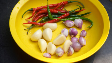 Shallots, garlic, red chilies, green chilies are all in a yellow plastic plate to be processed into cooking flavorings