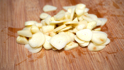 Onion slices with stenlis knife wooden table background. Sliced peeled garlic cloves are prepared as a cooking spice.
