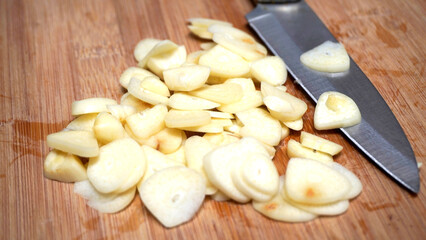 Onion slices with stenlis knife wooden table background. Sliced peeled garlic cloves are prepared as a cooking spice.
