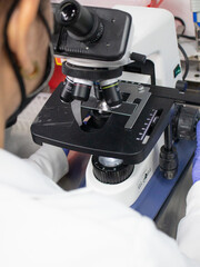 This photo shows a bioanalyst working in a laboratory. The bioanalyst is wearing a lab coat and safety glasses. They are using a microscope to examine a sample. The laboratory is well-lit and clean.