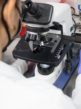 This photo shows a bioanalyst working in a laboratory. The bioanalyst is wearing a lab coat and safety glasses. They are using a microscope to examine a sample. The laboratory is well-lit and clean.