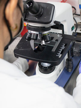 This photo shows a bioanalyst working in a laboratory. The bioanalyst is wearing a lab coat and safety glasses. They are using a microscope to examine a sample. The laboratory is well-lit and clean.