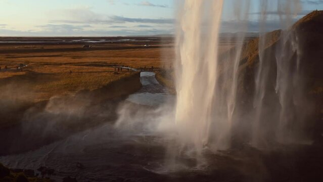 Spectacular waterfall at sunset. Huge flow of water seen from behind crossed by solar rays during golden hour. Seljalandsfoss, famous waterfall in southern Iceland 65 meters high. Slow motion 4k.