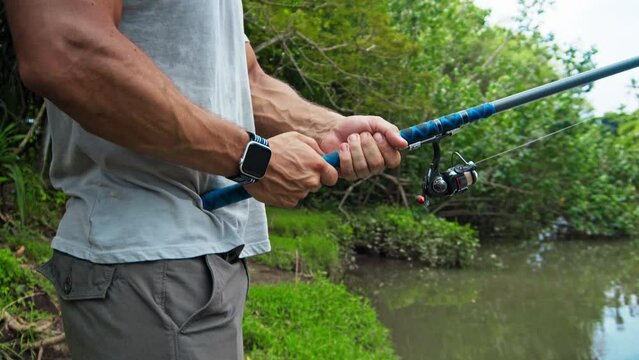 young guy with a fishing rod in his hands, twists a reel and fishes in a river in a rainforest.