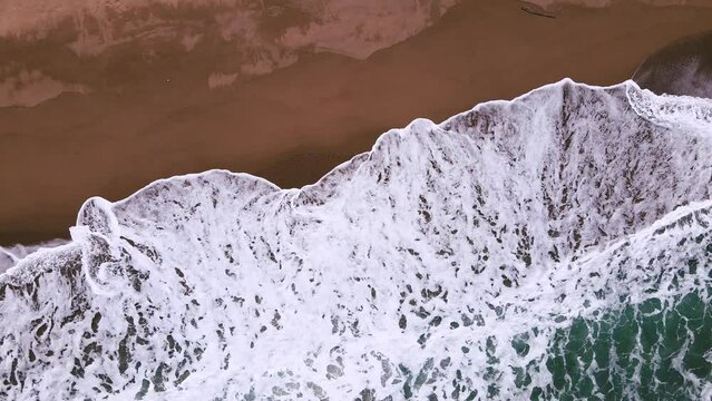 Slow motion sea waves with white foam on the sand beach aerial view camera tilt down