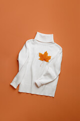 White warm sweater with autumn maple leaves on vivid orange color background, women jumper top view, minimal style trend autumn clothing concept, cozy clothes, two color Aesthetic Flat Lay