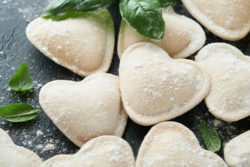 Italian ravioli pasta in heart shape. Tasty raw ravioli with flour and basil on dark background. Food cooking ingredients background. Valentines or Mothers Day lunch ideas. Top view with copy space.