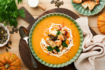 Pumpkin and carrot cream soup with herbs, seasonings and seeds in bowl on old wooden background in rustic style. Thanksgiving traditional autumn pumpkin cream soup. Top view. - obrazy, fototapety, plakaty