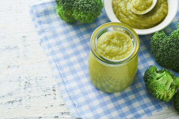 Green broccoli baby food in white bowl and jar on table. Green baby food. Child first feeding concept. Baby Natural Food. Production and menu of baby food. Selective focus.