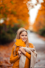 a teenage girl in a yellow sweater walks along a street outside the city against the backdrop of yellow trees. fun walk in autumn