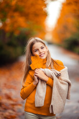 a teenage girl in a yellow sweater walks along a street outside the city against the backdrop of yellow trees. fun walk in autumn