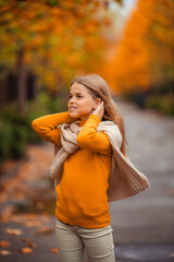 a teenage girl in a yellow sweater walks along a street outside the city against the backdrop of yellow trees. fun walk in autumn