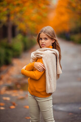 a teenage girl in a yellow sweater walks along a street outside the city against the backdrop of yellow trees. fun walk in autumn