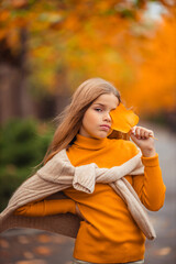 a teenage girl in a yellow sweater walks along a street outside the city against the backdrop of yellow trees. fun walk in autumn