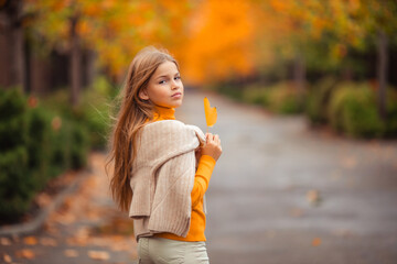 a teenage girl in a yellow sweater walks along a street outside the city against the backdrop of yellow trees. fun walk in autumn
