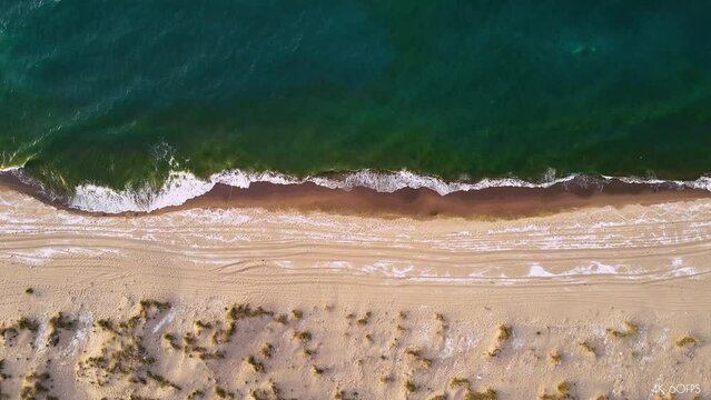 Slow motion sea waves green blue water on the sand beach with jeep tyre trails aerial view camera tilt down 