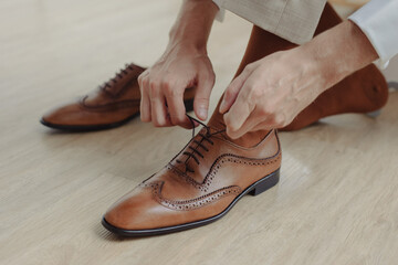 groom binding brown leather shoes on the floor