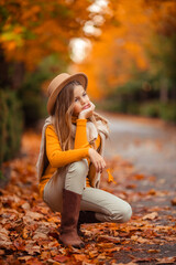 a teenage girl in a yellow sweater walks along a street outside the city against the backdrop of yellow trees. fun walk in autumn