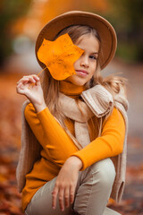 a teenage girl in a yellow sweater walks along a street outside the city against the backdrop of yellow trees. fun walk in autumn