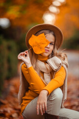 a teenage girl in a yellow sweater walks along a street outside the city against the backdrop of yellow trees. fun walk in autumn