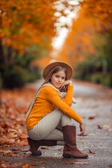 a teenage girl in a yellow sweater walks along a street outside the city against the backdrop of yellow trees. fun walk in autumn