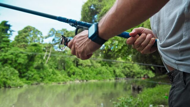 young guy with a fishing rod in his hands, twists a reel and fishes in a river in a rainforest.