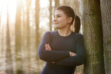 Athletic young sporty woman after workout, running and exercises leaning relaxed on a tree on a...