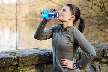 Sporty and athletic woman running and jogging drinking water from a bottle on a sunny winter morning in a forest - 673940296