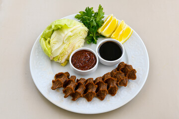 Cig kofte (raw meatball) with lettuce, tomato, pickle and lemon, hot Chee kofta. Turkish local raw food concept.Table scene of assorted take out or delivery foods. Doritoslu cig kofte durum.