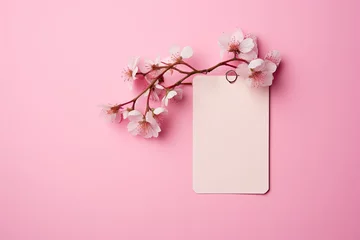 Foto op Canvas A light label or tag from clothing hangs on a branch of a blossoming cherry tree with a pink background. Blank space for promotional text or discount. © OleksandrZastrozhnov