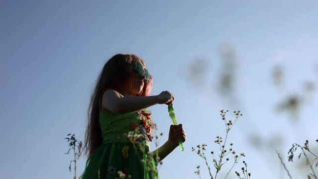 Redhead girl dressed as a fairy blowing bubbles outdoors. Cute white child celebrates St. Patrick's Day