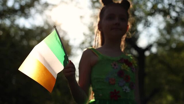 Cute leprechaun girl waving with flag of Ireland in slow motion. Adorable red head girl celebrating St. Patrick's Day on the 17th of March