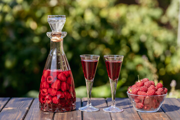 Homemade red raspberry brandy in two glasses and in a glass bottle on a wooden table in a summer...